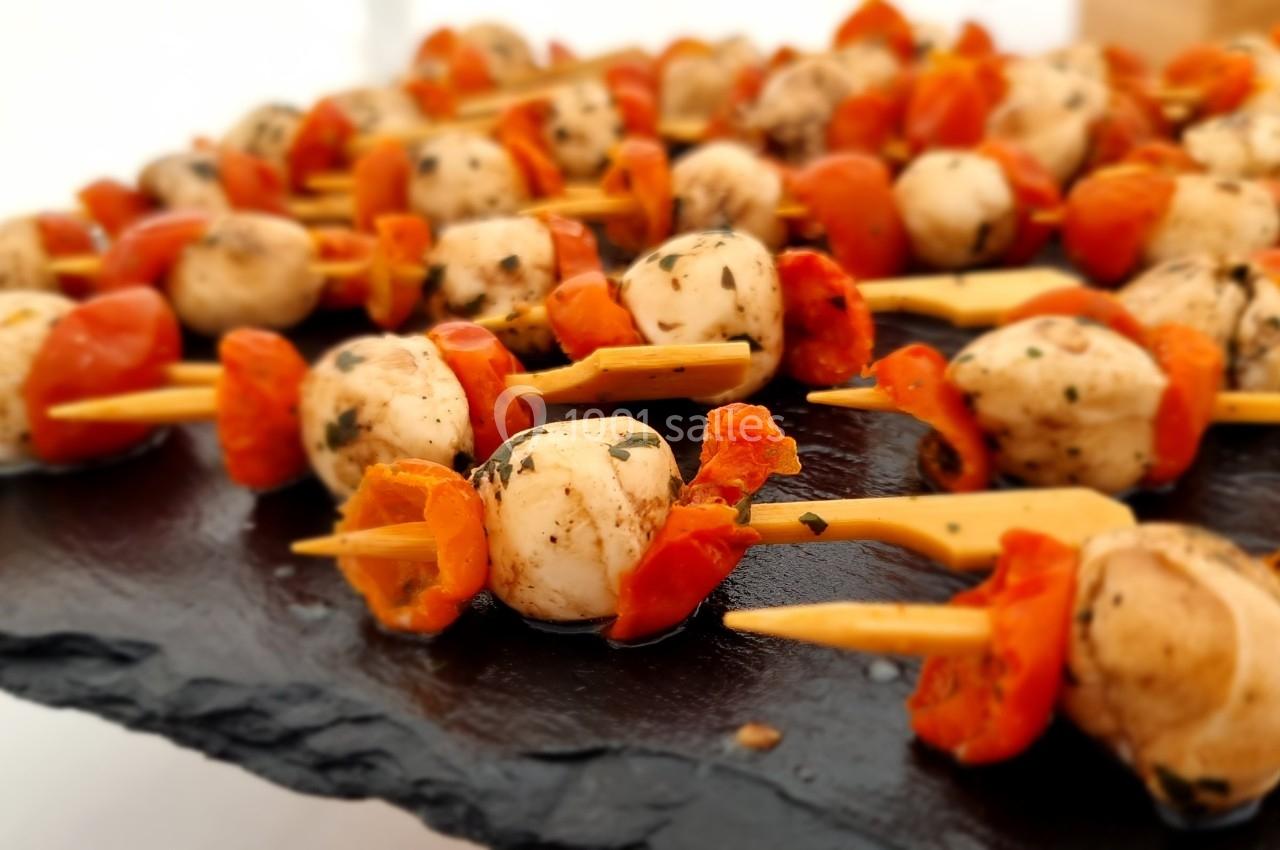 Brochettes apéritives composées de tomates cerises, champignons et herbes, présentées sur une ardoise noire.