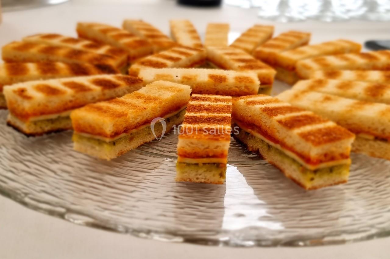 Assortiment de sandwichs grillés coupés en rectangles, disposés en cercle sur une assiette en verre.