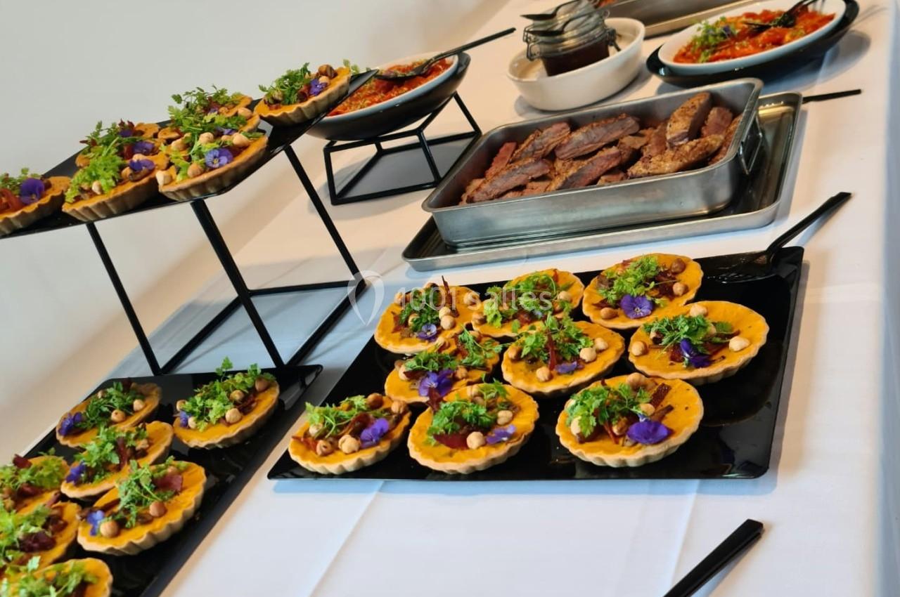 Buffet varié avec tartelettes garnies, salades colorées et plats chauds disposés sur une table blanche.