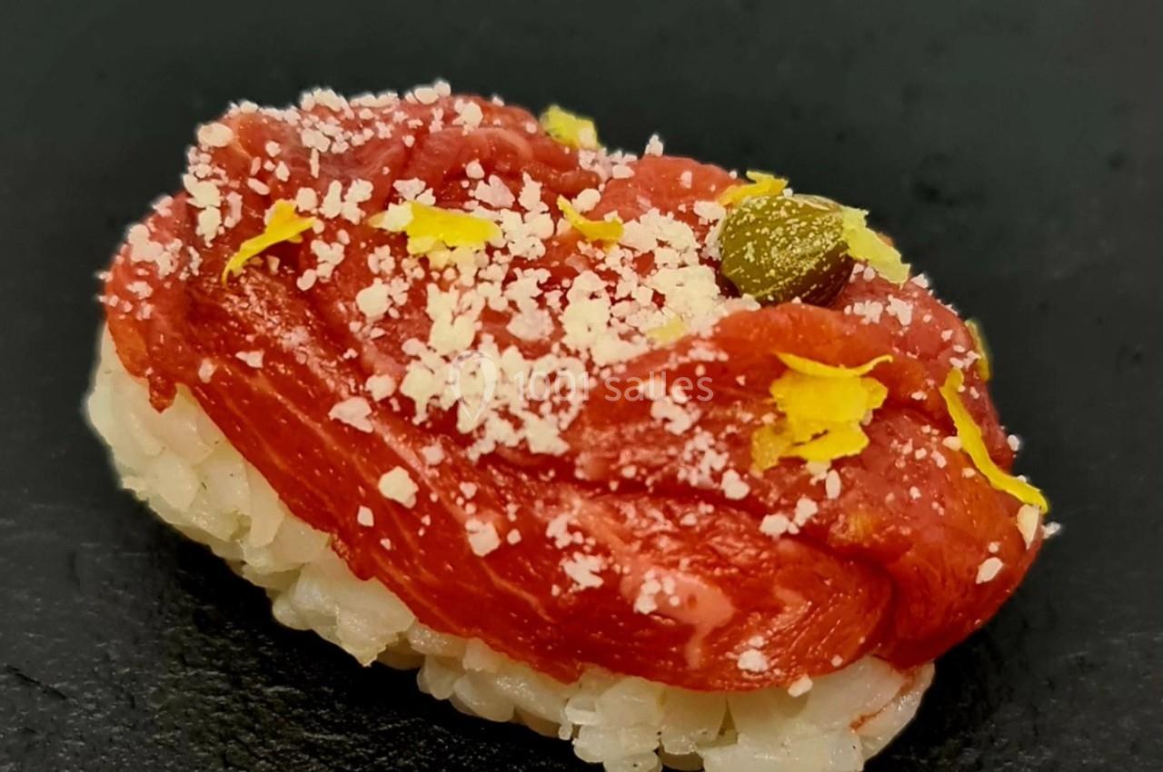 Nigiri composé de riz vinaigré, surmonté de viande rouge crue, de copeaux de fromage et de zestes jaunes.