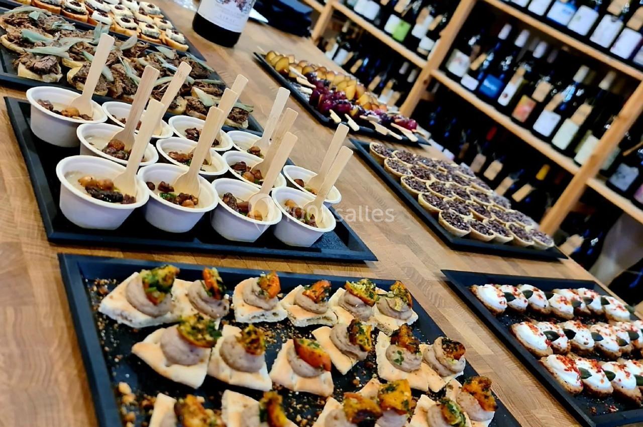 Plateaux de bouchées apéritives variées disposés sur une table en bois, avec des bouteilles de vin en arrière-plan.
