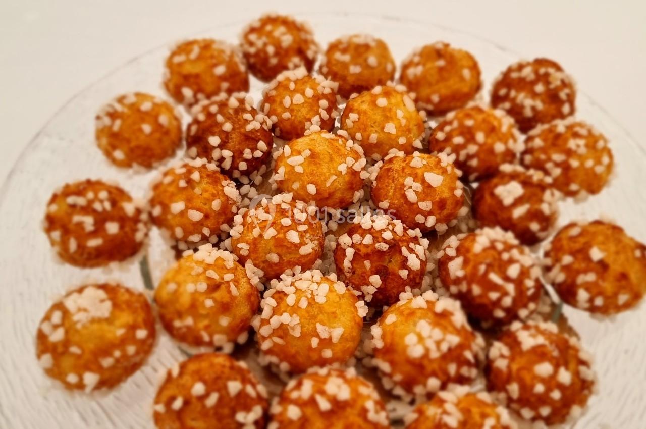 Assortiment de chouquettes dorées garnies de grains de sucre sur une assiette en verre.