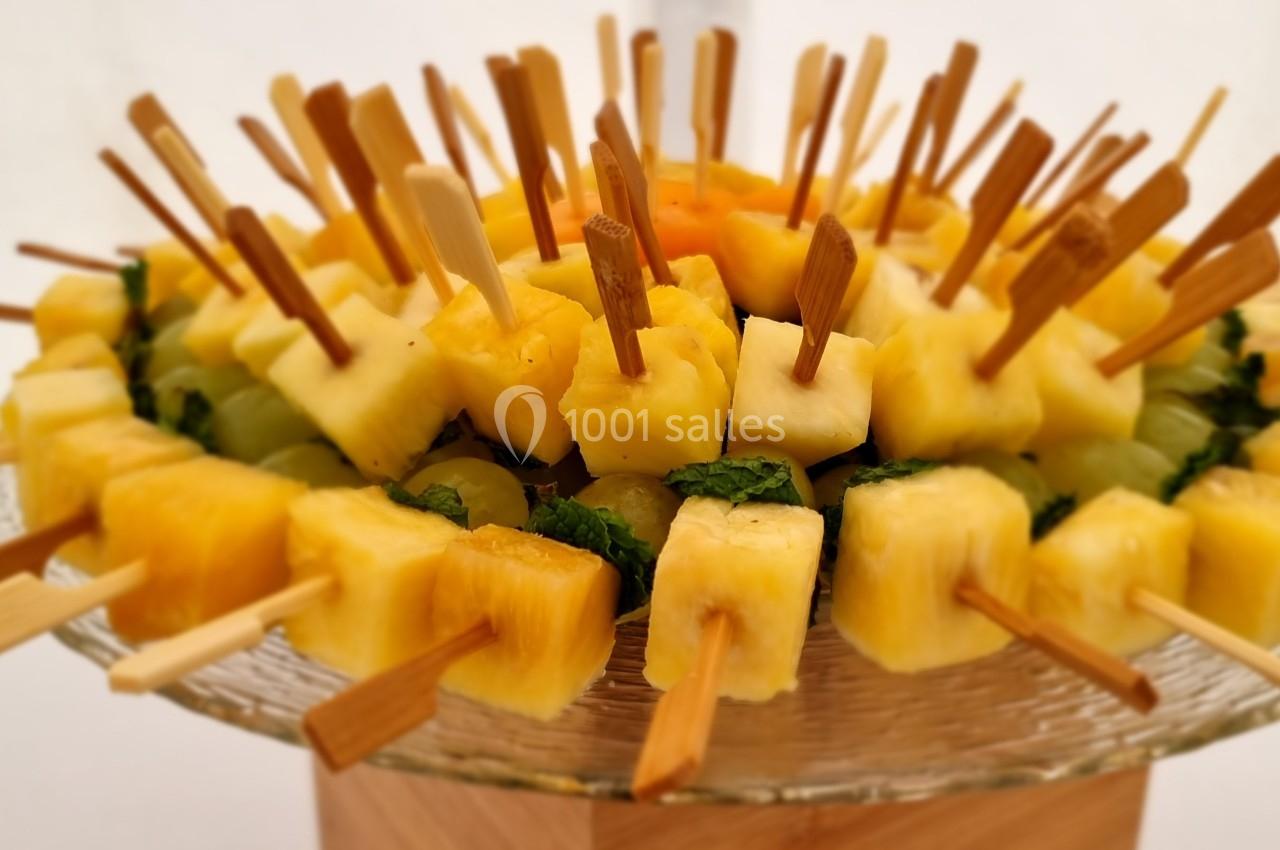 Brochettes de fruits composées d'ananas et de morceaux colorés, présentées sur un plat en verre.