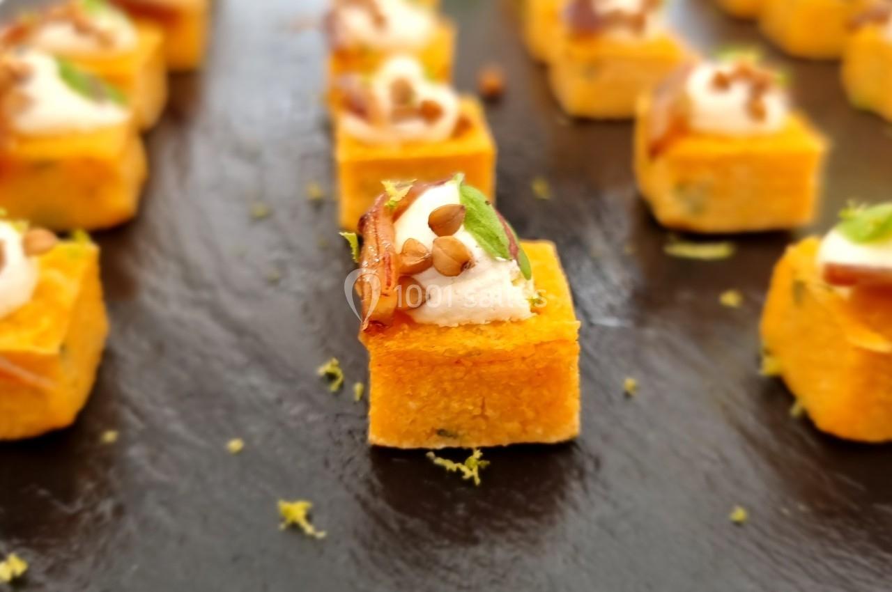 Bouchées apéritives sur une ardoise, composées de cubes dorés garnis de crème, herbes et éclats croustillants.