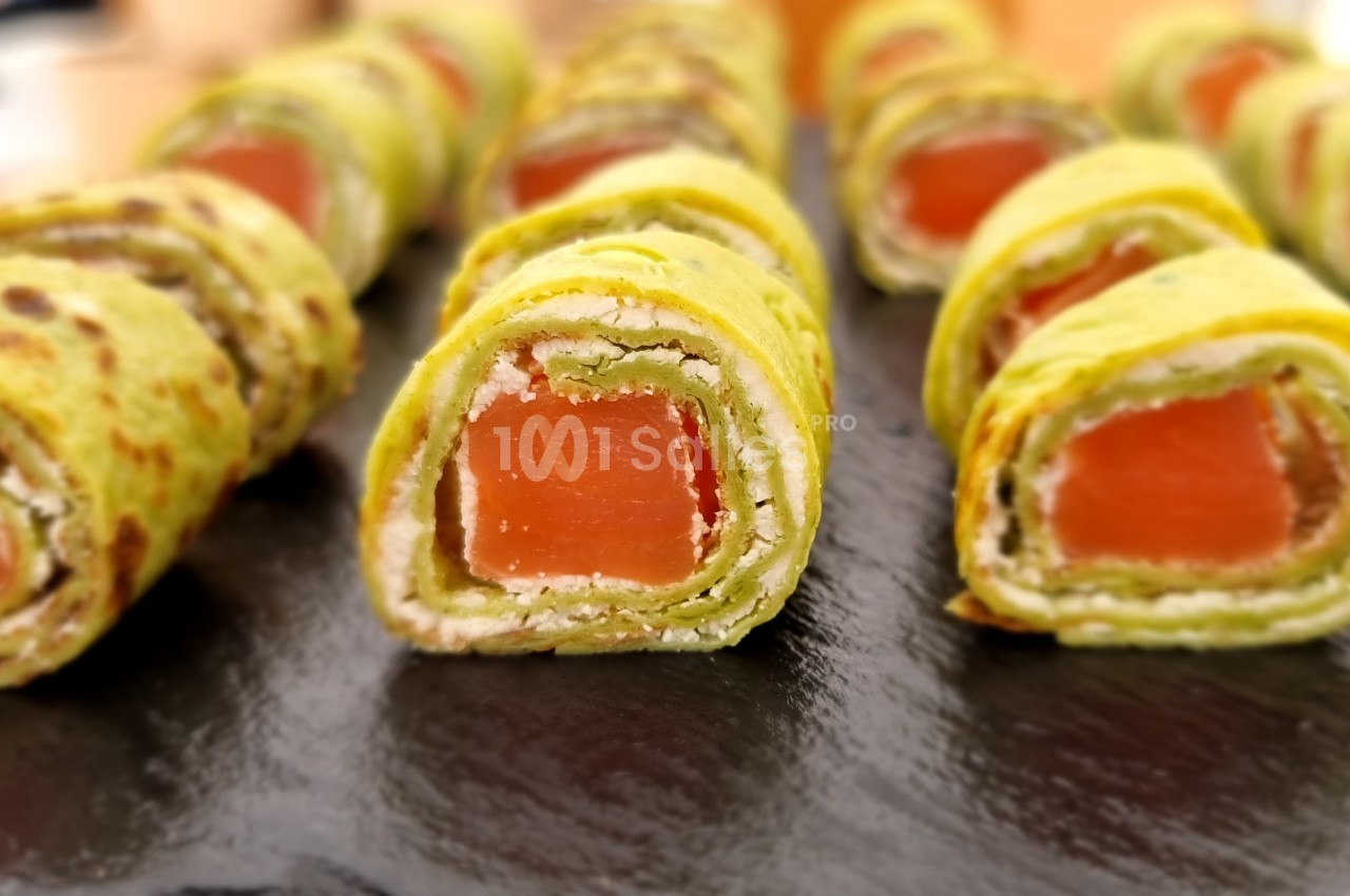 Roulés de crêpes vertes garnis de saumon fumé et fromage frais, présentés sur une ardoise noire.