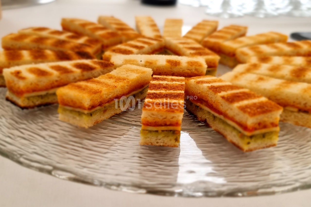 Assortiment de mini-sandwichs grillés disposés en cercle sur une assiette en verre transparente.