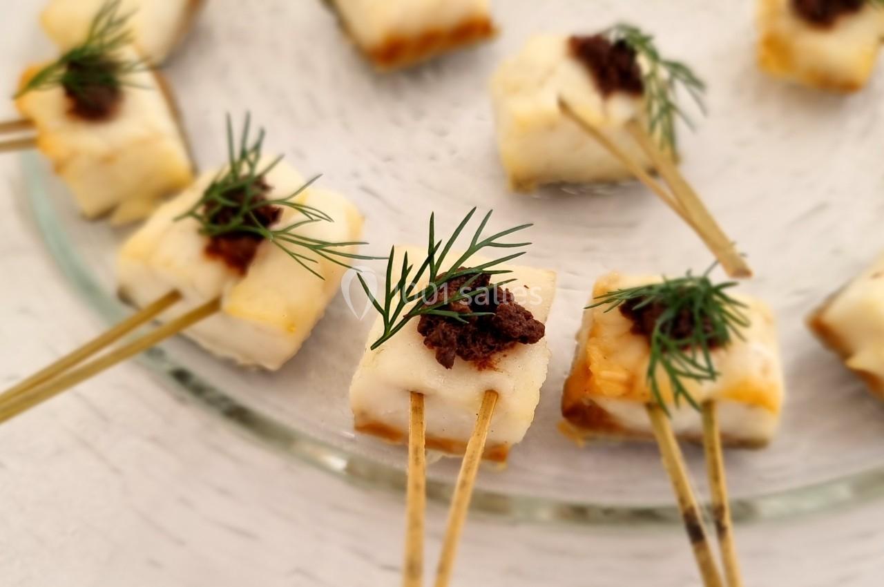 Bouchées apéritives sur piques en bois, garnies de fromage, tapenade et brins d'aneth, disposées sur une assiette en verre.