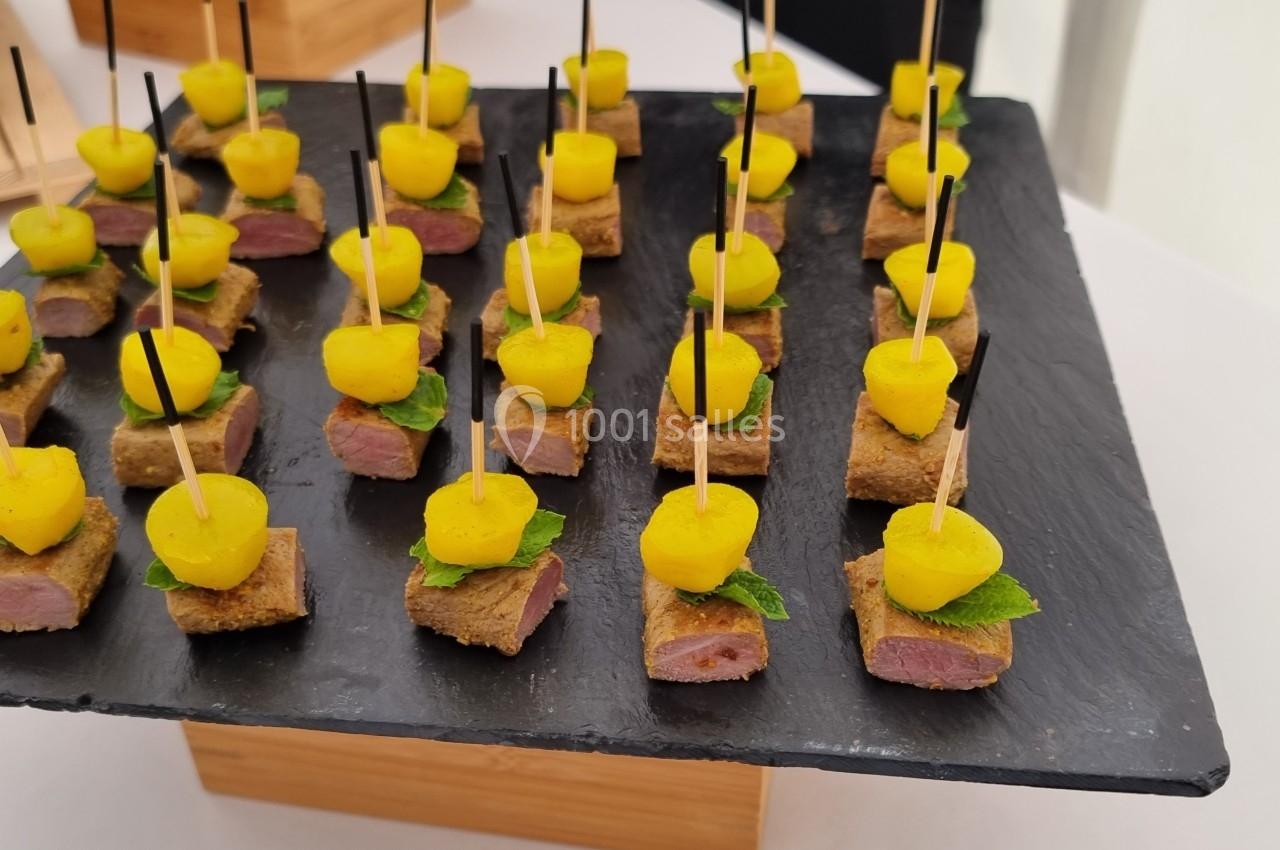 Plateau d'amuse-bouches composés de morceaux de viande, cubes de pain, billes jaunes et feuilles de menthe, présentés sur…