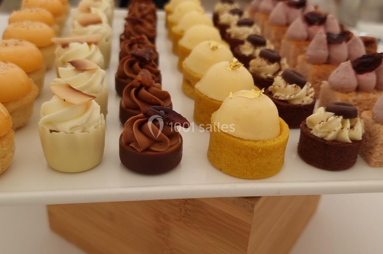 Plateau de mignardises variées disposées en rangées, comprenant des gâteaux et crèmes décorés.