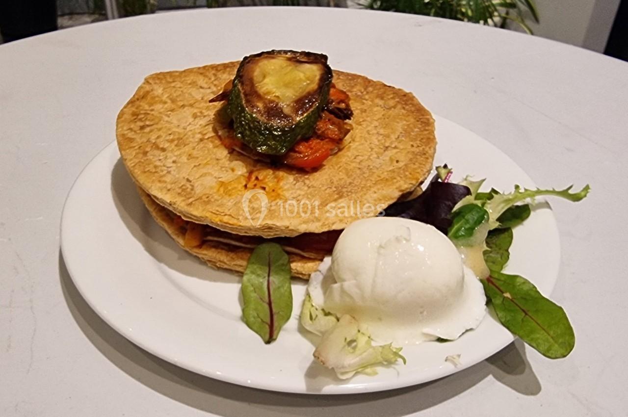Plat composé de galettes empilées garnies de légumes grillés, accompagné de salade verte et d'une boule de fromage frais.