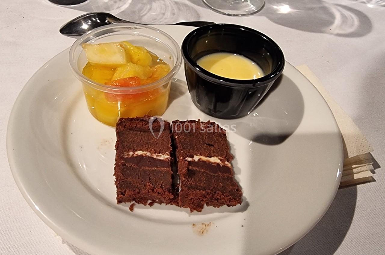 Assiette contenant deux tranches de gâteau au chocolat, une verrine de fruits et une coupelle de crème anglaise.