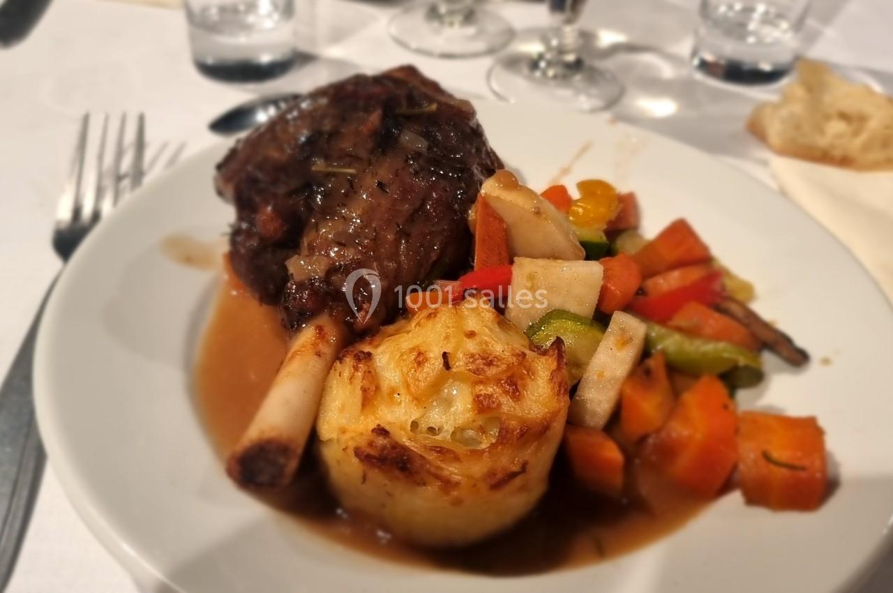 Assiette contenant une pièce de viande en sauce, un gratin de pommes de terre et des légumes colorés, servie sur une table…