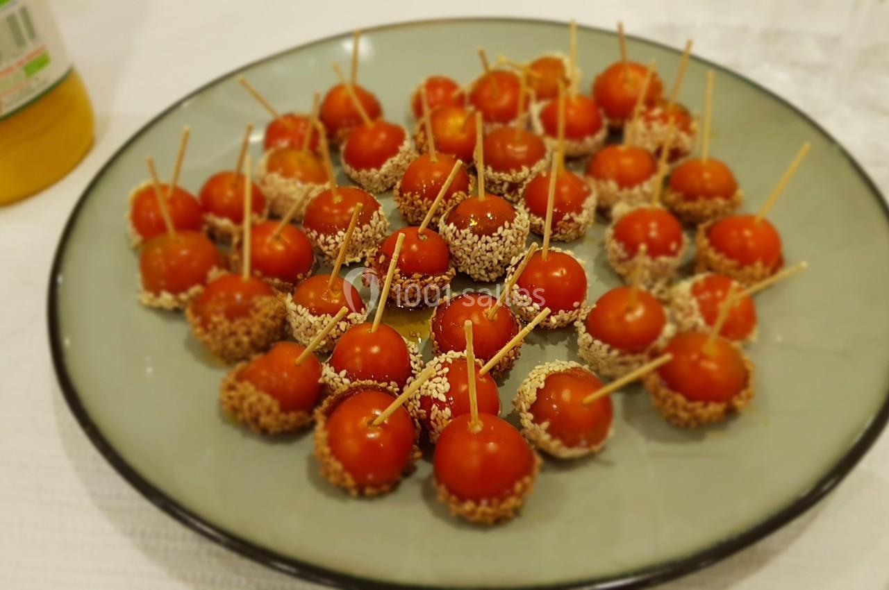 Tomates cerises en brochettes, enrobées de graines de sésame, disposées sur une assiette ronde.