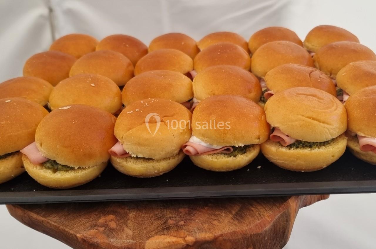 Plateau de mini-sandwichs garnis de jambon et de sauce verte, disposés sur un support en bois.