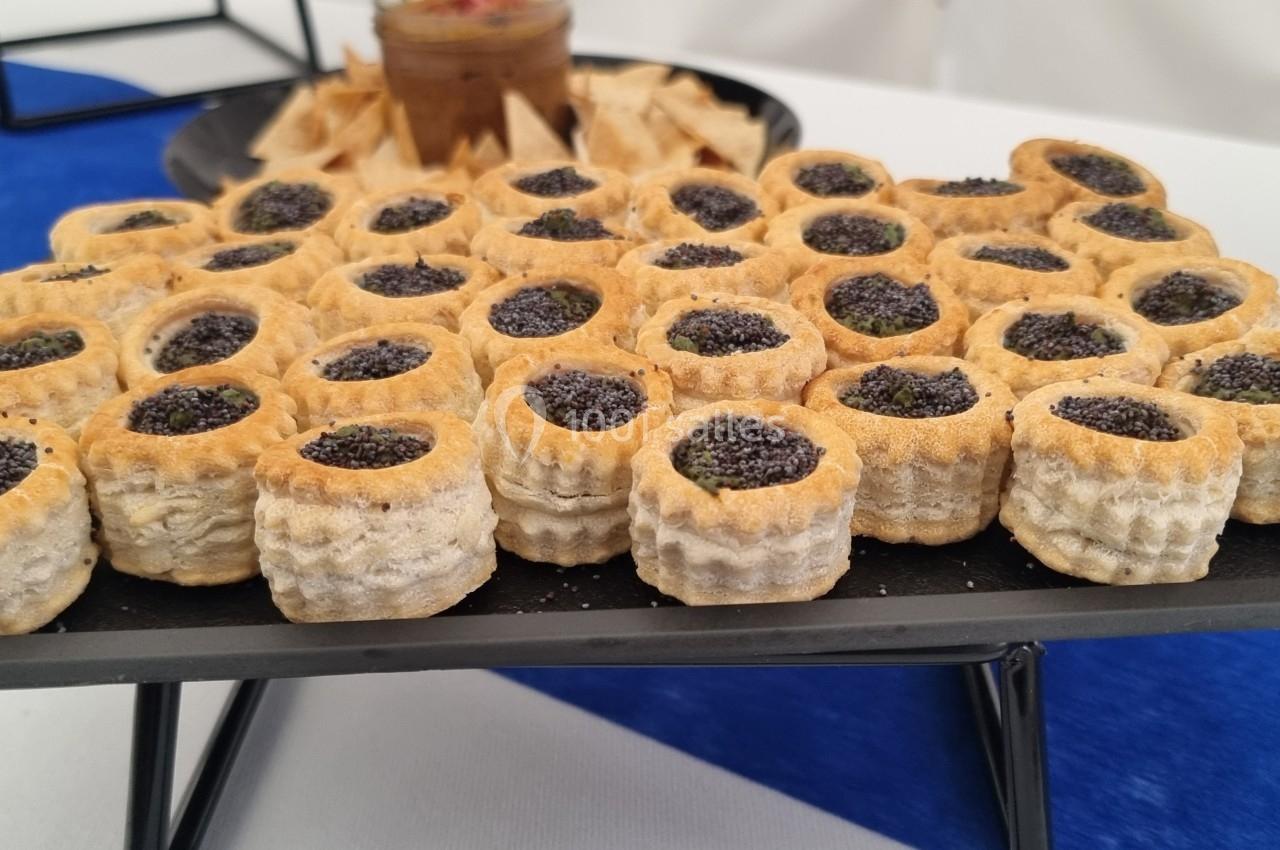 Plateau de bouchées feuilletées garnies de graines de pavot, disposé sur une table avec nappe bleue et blanche.