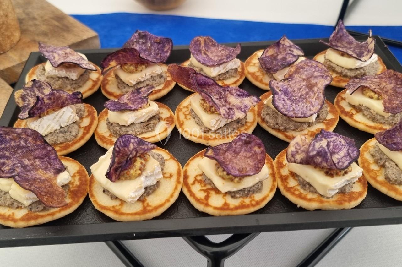 Plateau de mini-blinis garnis de fromage, tapenade et chips de pommes de terre violettes.