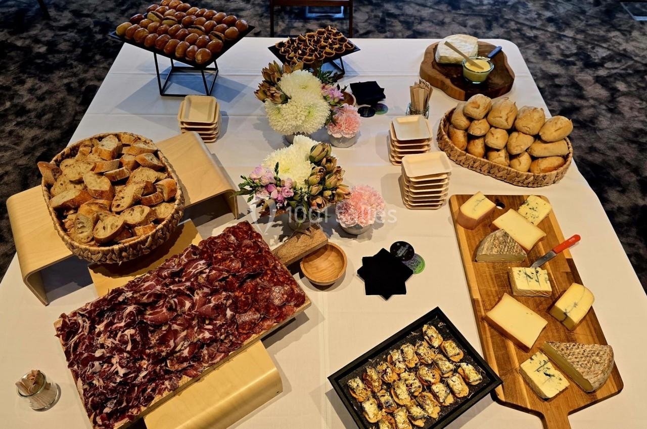 Table dressée avec charcuterie, fromages, pains, amuse-bouches et décorations florales sur une nappe blanche.