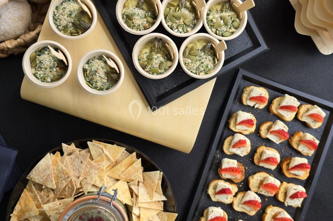 Buffet composé de verrines, toasts, chips avec sauce, pains et mini-burgers disposés sur une table noire.