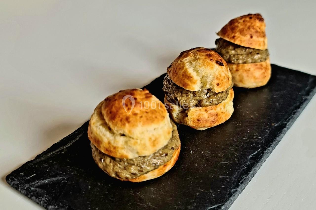 Trois petits choux garnis de mousse ou tapenade, disposés sur une ardoise noire.