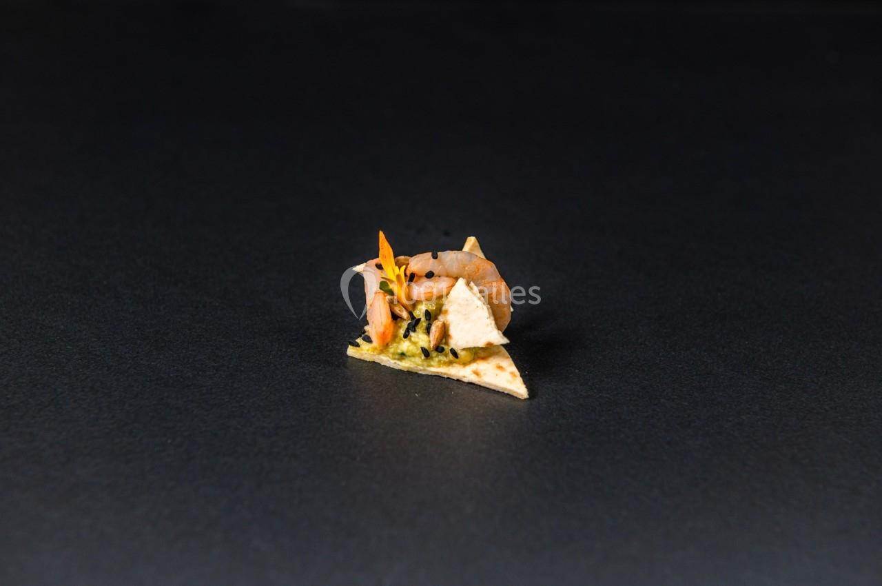 Un petit crabe posé sur un morceau de tortilla garni de guacamole, sur un fond noir uni.