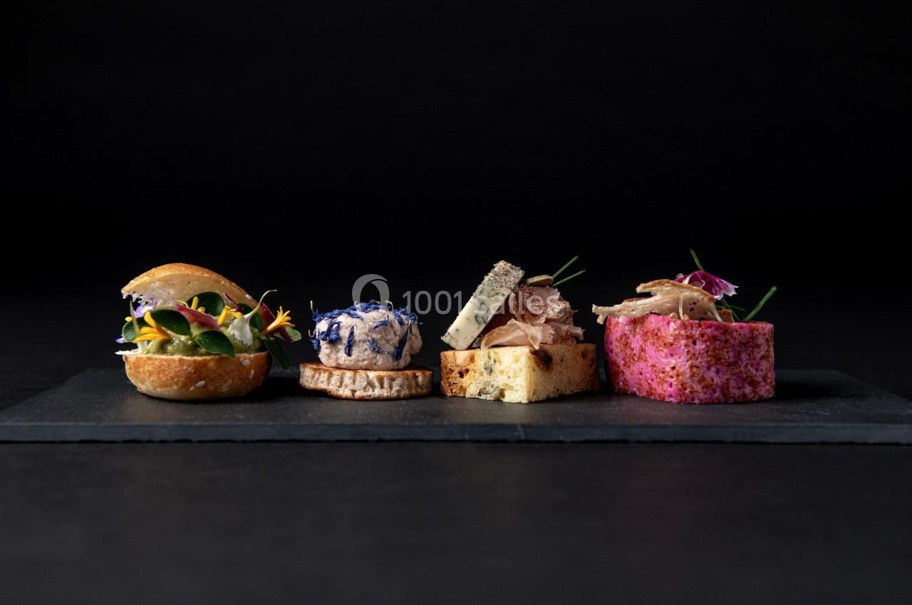 Assortiment de bouchées gastronomiques colorées disposées sur une ardoise noire, en fond sombre.