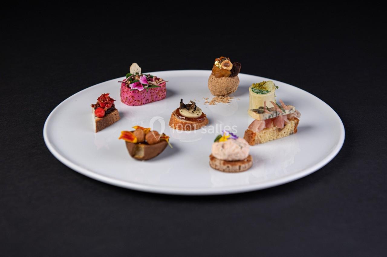 Assortiment de bouchées gastronomiques variées présentées sur une assiette blanche, fond noir.