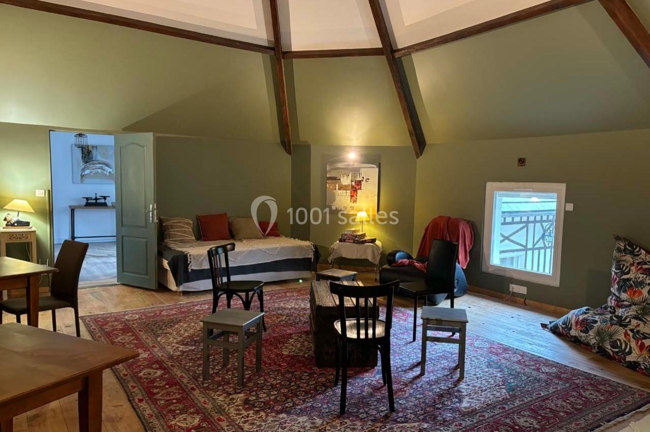 Salon spacieux avec murs verts, tapis rouge, meubles variés et lumière naturelle entrant par une petite fenêtre.