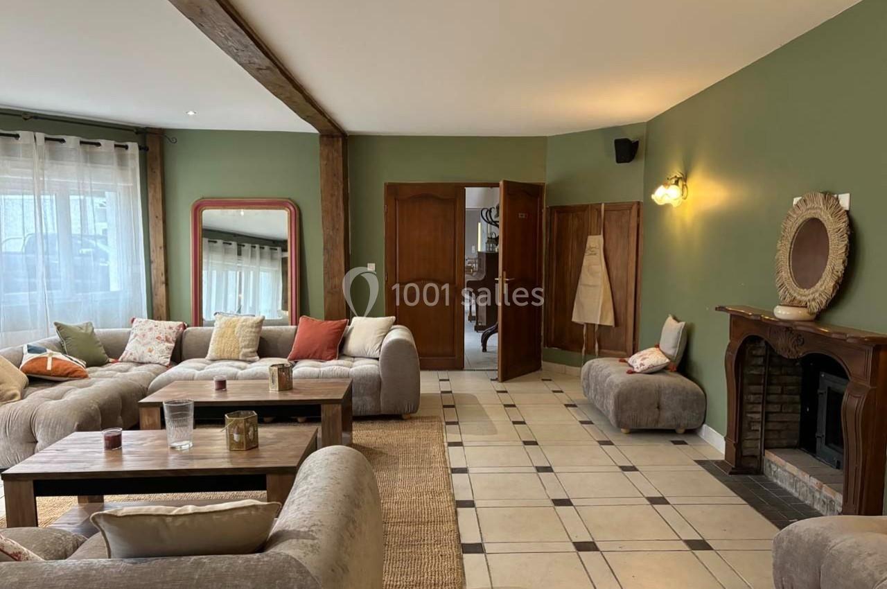Salon chaleureux avec murs verts, canapés beiges, cheminée en bois, miroir et table basse en bois sur tapis clair.