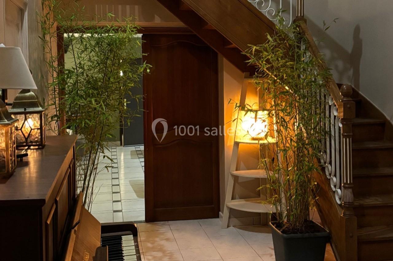 Vue d'un hall d'entrée avec un escalier en bois, des plantes en pot, un piano et un éclairage chaleureux.