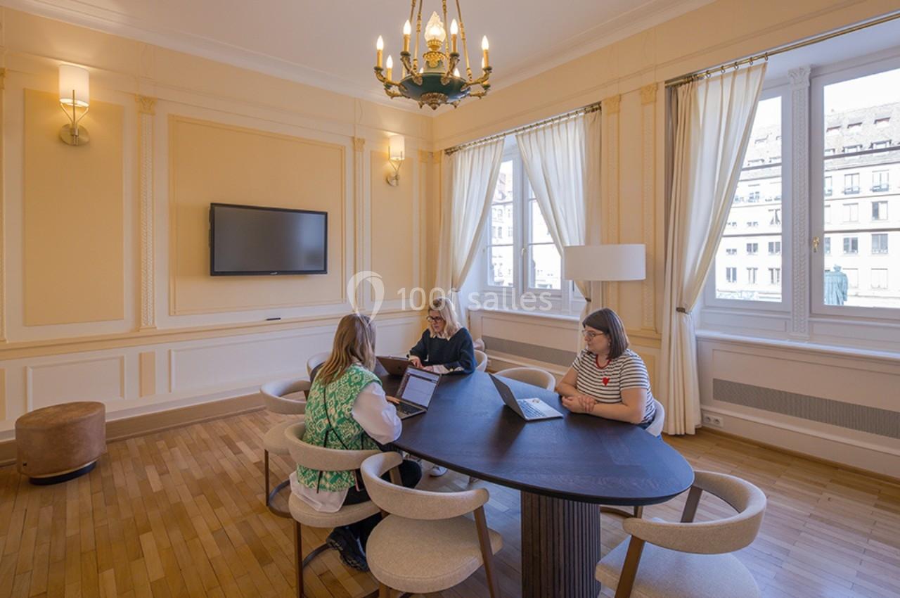 Trois personnes travaillent sur des ordinateurs portables autour d'une table ovale dans une salle lumineuse avec des…