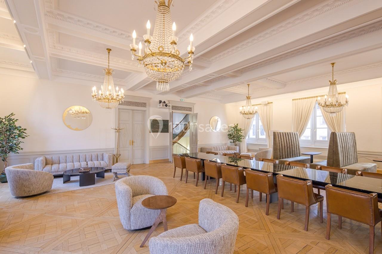 Salle lumineuse avec parquet en bois, lustres élégants, fauteuils modernes, tables et chaises en cuir disposées…