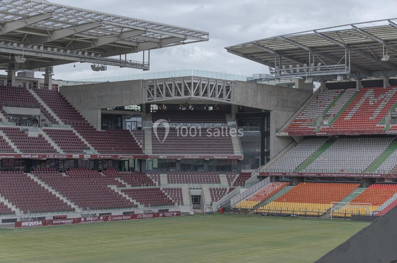 Vue d'un stade vide avec des gradins multicolores et une structure en béton sous un ciel nuageux.