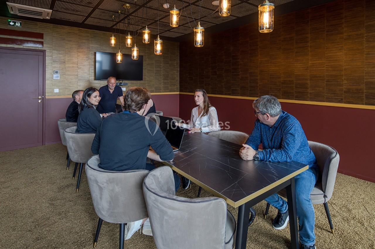 Des personnes assises autour d'une table dans une salle de réunion avec un écran mural et des luminaires suspendus.
