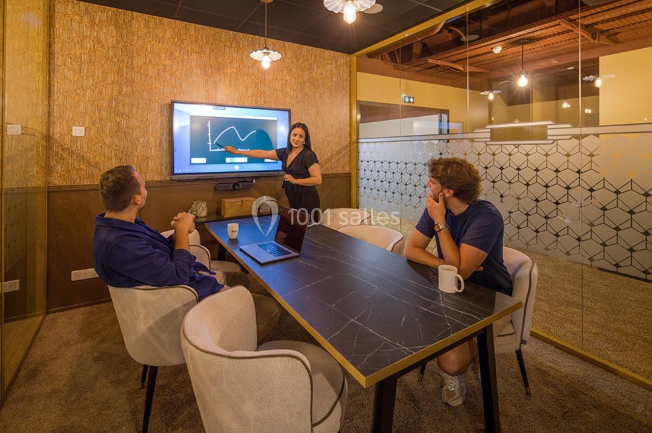 Une femme présente un graphique sur un écran à deux collègues assis autour d'une table dans une salle de réunion moderne.