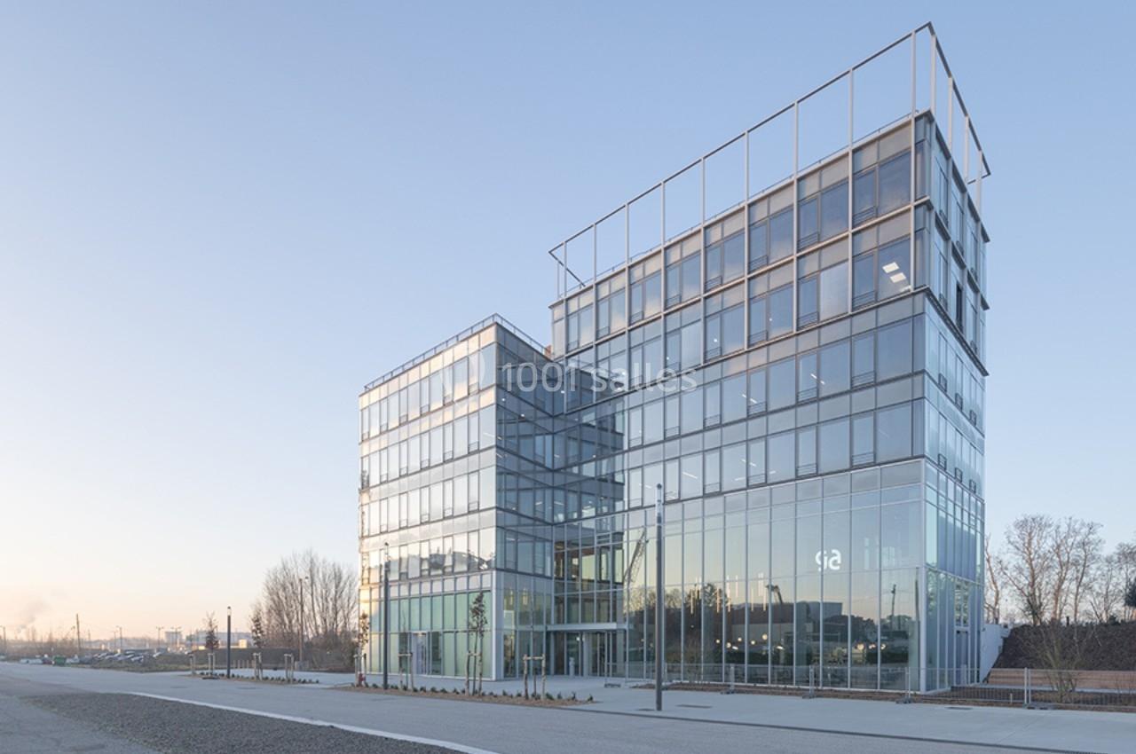 Bâtiment moderne en verre et acier avec plusieurs étages, situé dans un environnement urbain dégagé.