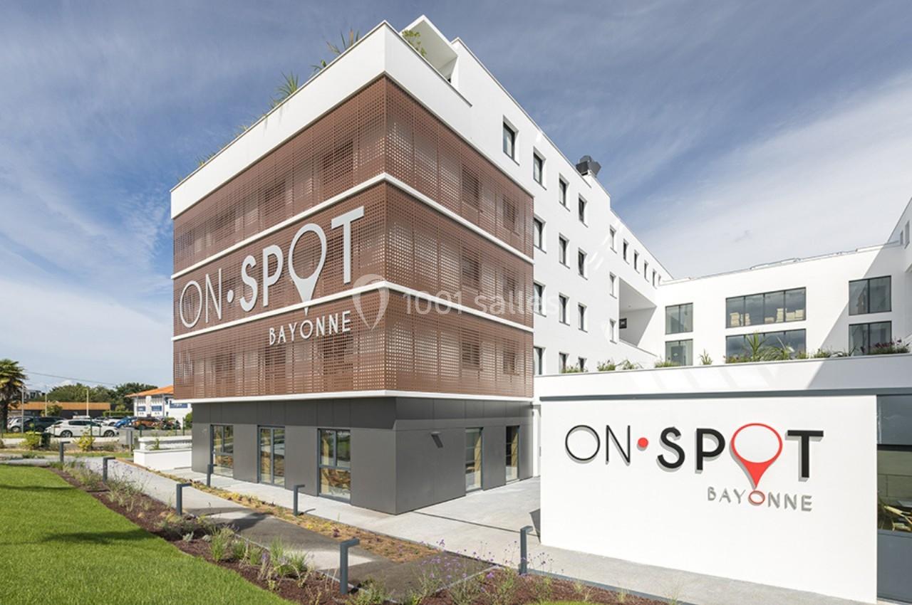 Façade moderne d'un bâtiment blanc avec des panneaux en bois et le logo ’On Spot Bayonne’ visible.