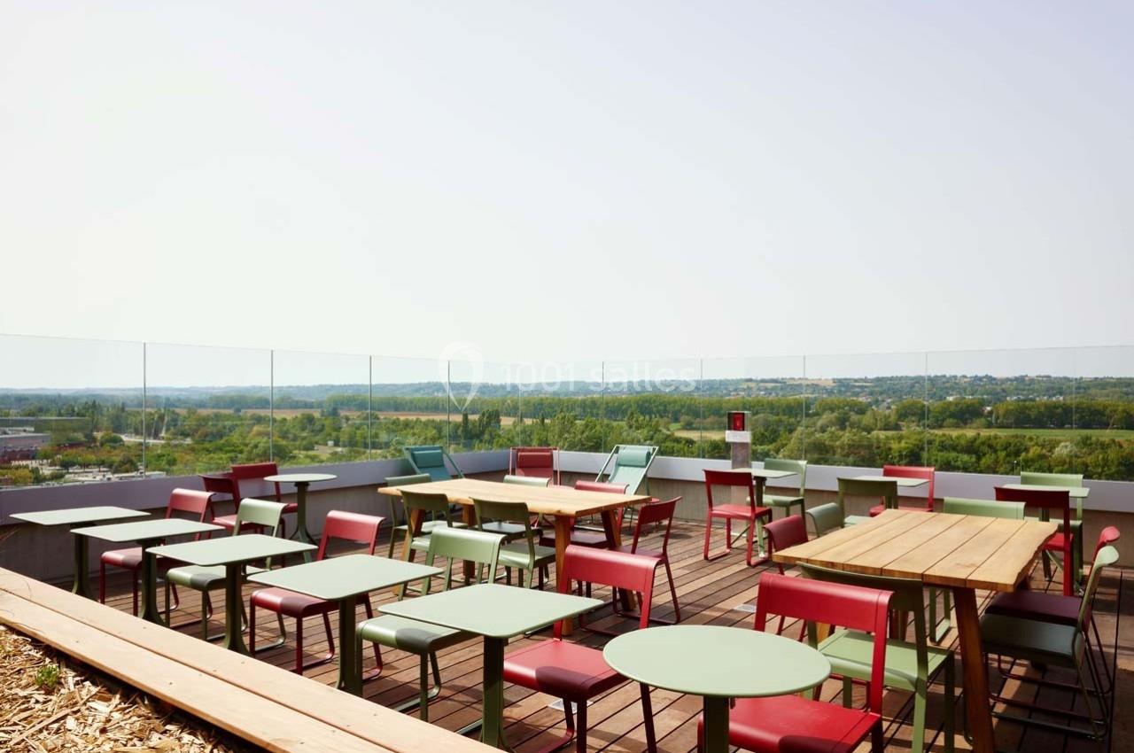 Terrasse en hauteur avec tables et chaises colorées, offrant une vue dégagée sur un paysage verdoyant.