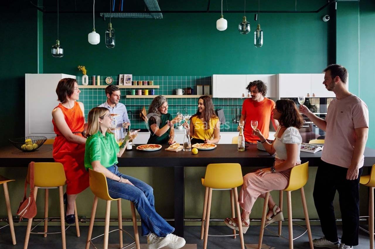 Un groupe de personnes assises et debout autour d'un comptoir dans une cuisine moderne, partageant un repas et discutant.
