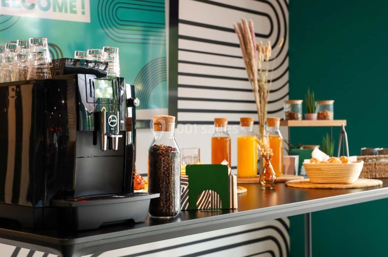 Machine à café noire et buffet avec boissons, viennoiseries et décorations dans un espace moderne et coloré.