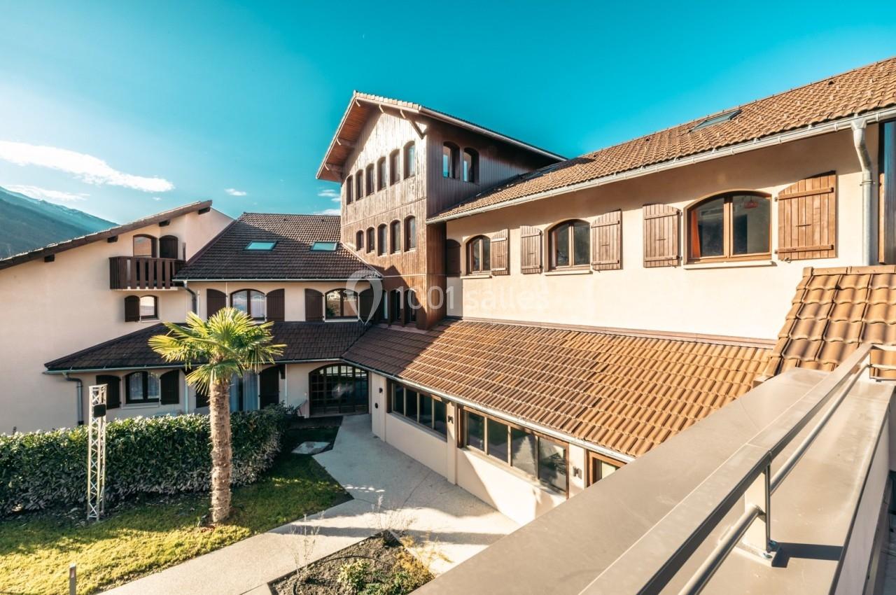 Bâtiment ensoleillé avec façade beige, volets en bois, toit en tuiles et une palmeraie au premier plan.