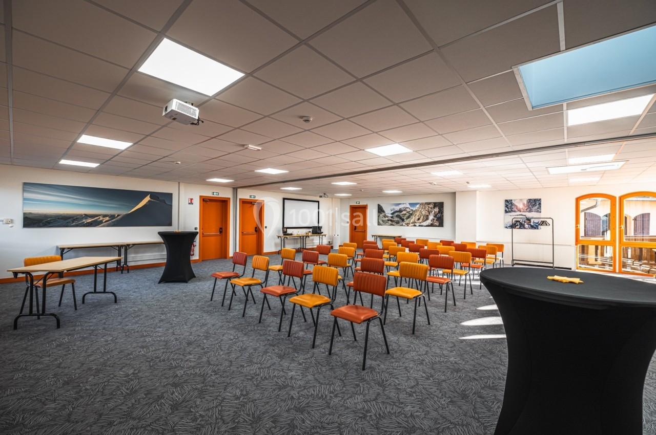Salle de conférence lumineuse avec des rangées de chaises colorées, un projecteur et des tables disposées à l'avant.