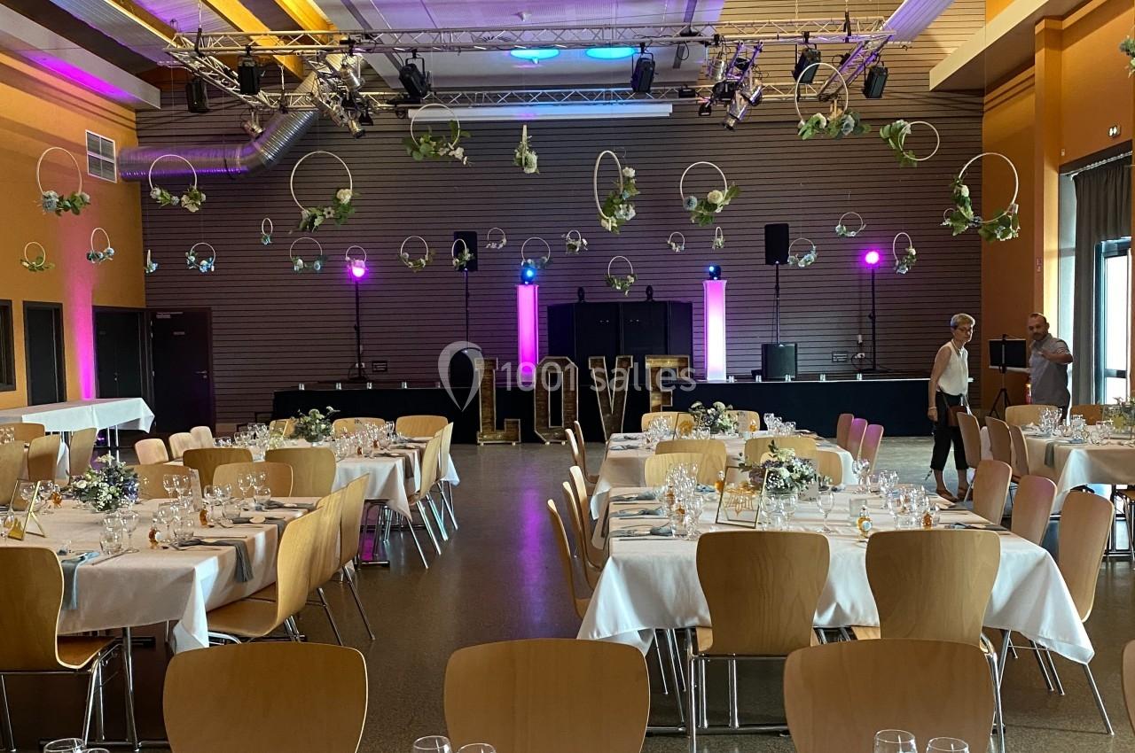 Salle de réception décorée pour un mariage, avec tables dressées, lettres ’LOVE’ lumineuses et suspensions florales.