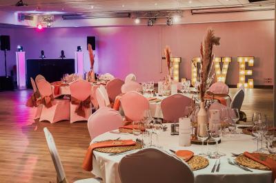 Salle de réception lumineuse avec tables rondes dressées, grandes baies vitrées et structure métallique apparente.