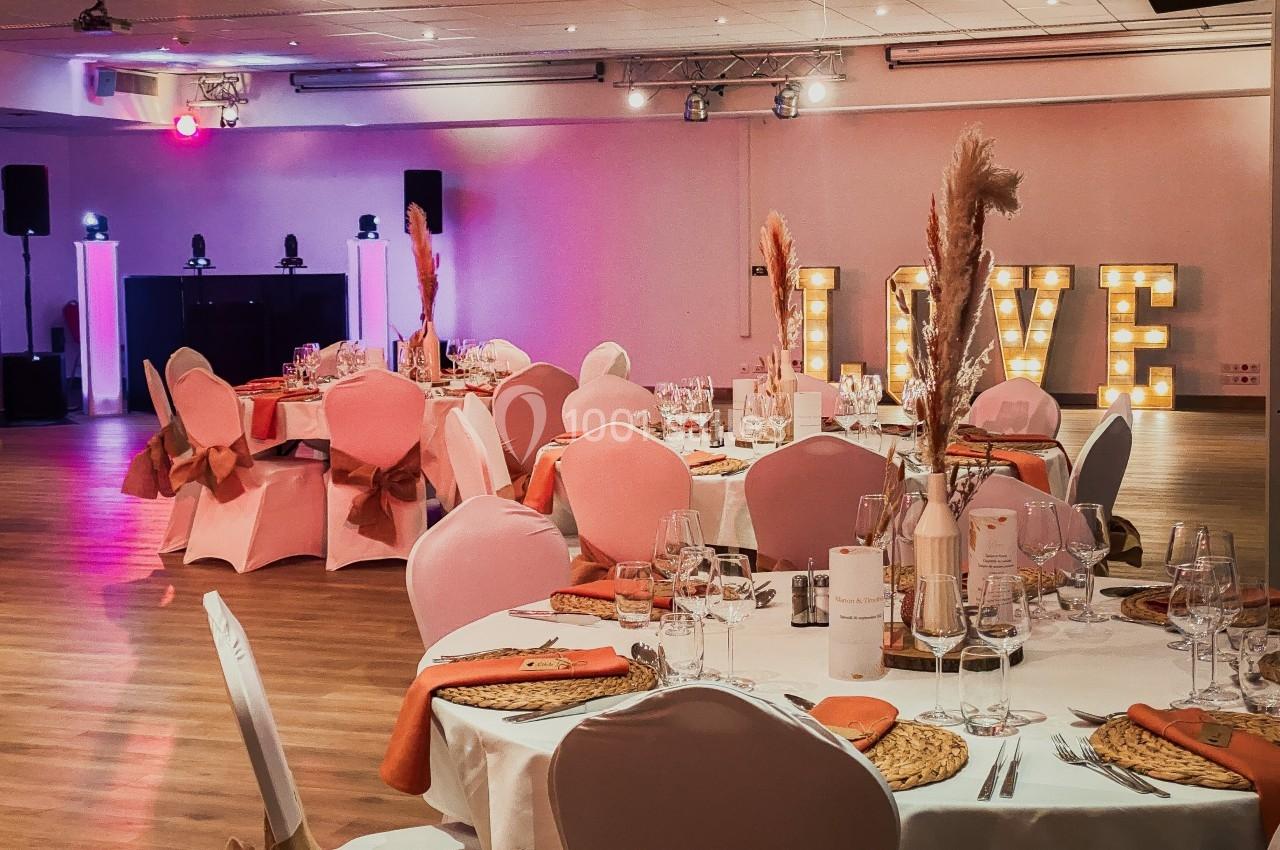 Salle de réception décorée avec des tables dressées, des chaises roses et des lettres lumineuses formant ’LOVE’.