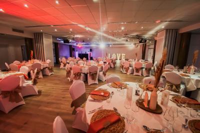 Salle de réception lumineuse avec tables rondes dressées, grandes baies vitrées et structure métallique apparente.