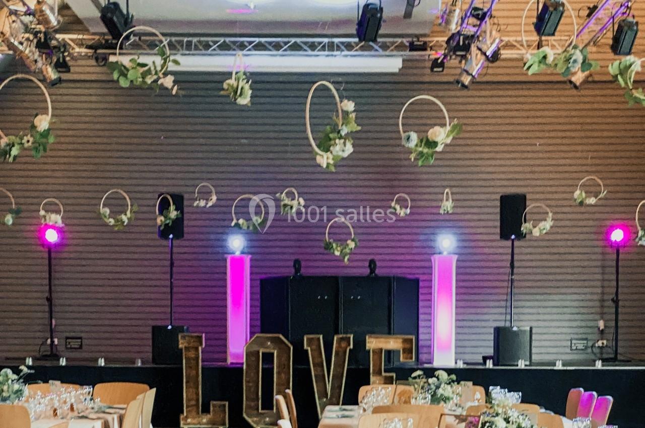 Salle décorée pour un événement avec des fleurs suspendues, des lettres géantes formant ’LOVE’ et un éclairage coloré.