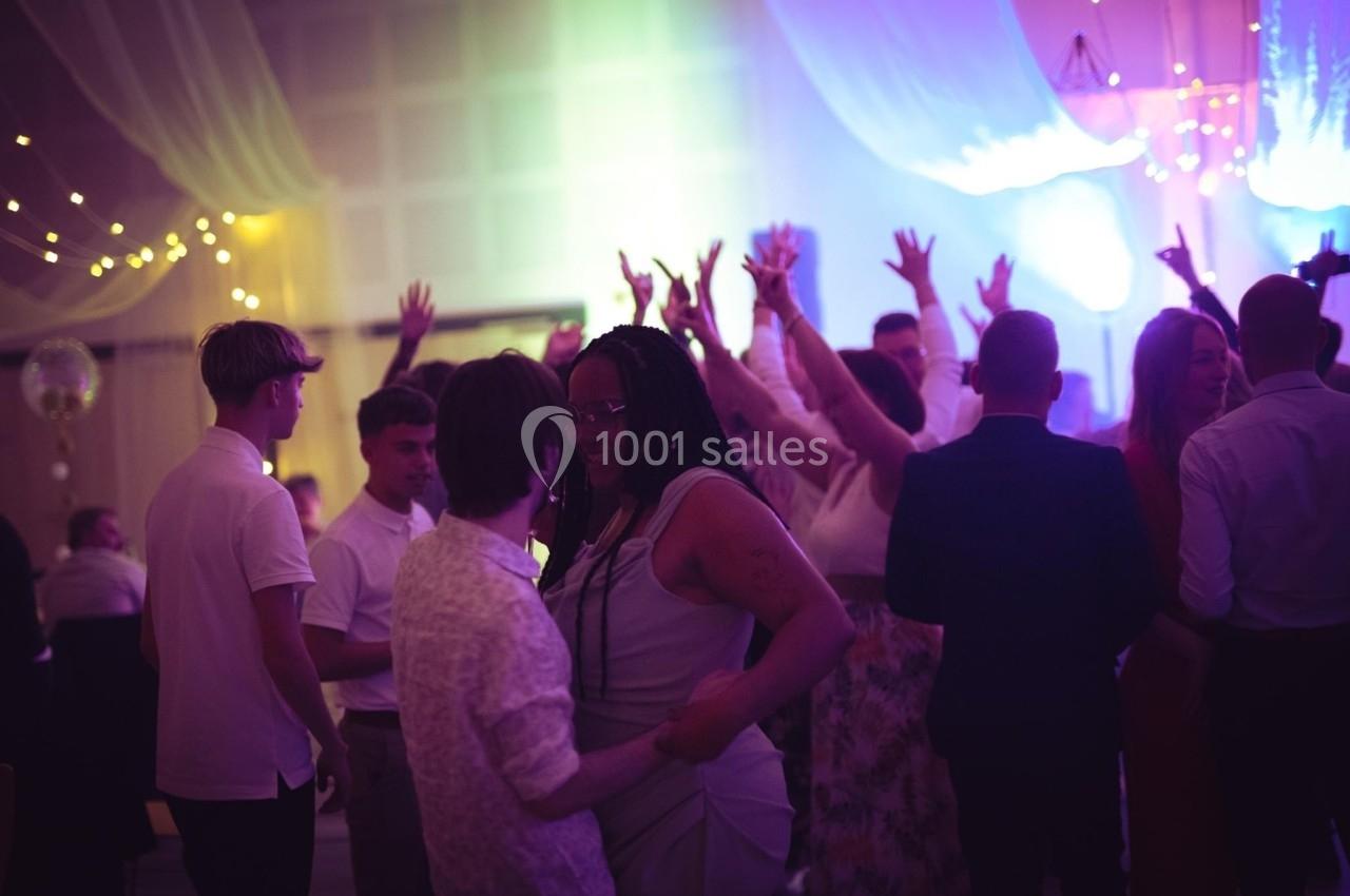 Des personnes dansent et discutent dans une salle décorée de lumières colorées et d'étoffes suspendues.