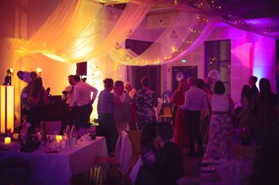 Salle de réception lumineuse avec tables rondes dressées, grandes baies vitrées et structure métallique apparente.