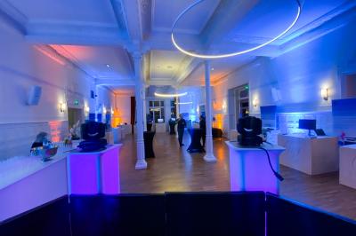 Salle de réception lumineuse avec tables rondes dressées, grandes baies vitrées et structure métallique apparente.