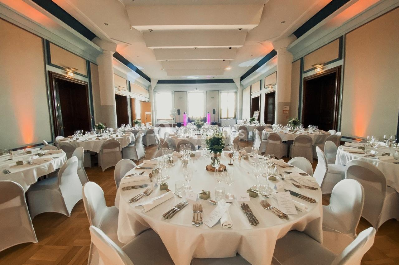 Salle de réception élégante avec tables rondes dressées, nappes blanches et éclairage chaleureux.
